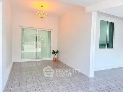 Spacious tiled room with chandelier and sliding glass doors, perfect for versatile living space.