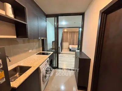 Modern apartment with sleek kitchen and washing machine, leading to a cozy bedroom.