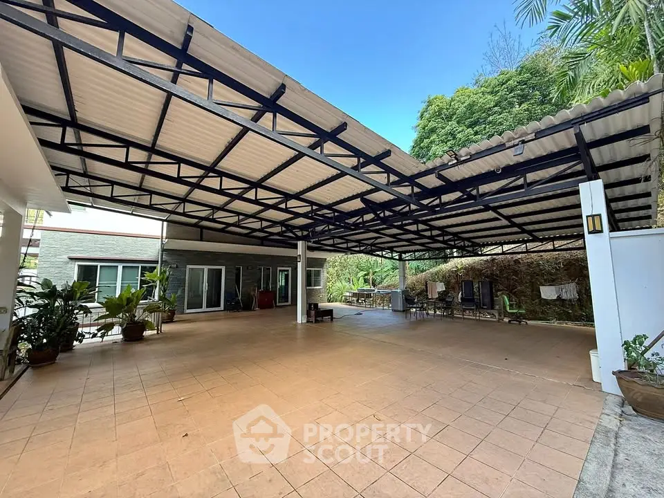 Spacious covered outdoor area with tiled flooring and lush greenery.