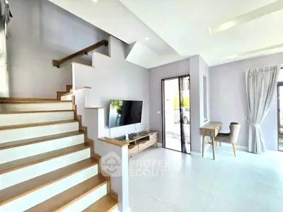 Modern living room with staircase and natural light, featuring sleek furniture and open layout.