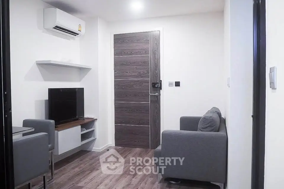 Modern living room with sleek furniture and wooden flooring, featuring a mounted TV and air conditioning.
