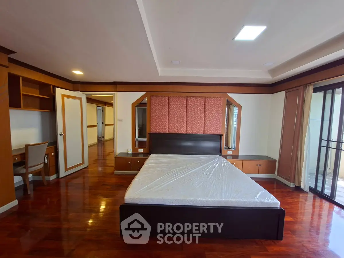 Spacious bedroom with elegant wooden flooring and large windows for natural light.