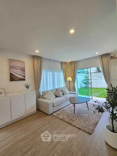 Modern living room with large windows and garden view, featuring cozy sofa and stylish decor.