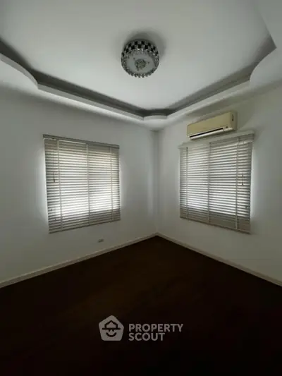Spacious and well-lit empty room with polished wooden floors, two large windows with blinds, and an elegant ceiling design with a modern light fixture.