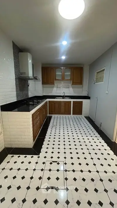 Spacious kitchen with elegant black and white tile flooring and wooden cabinetry.