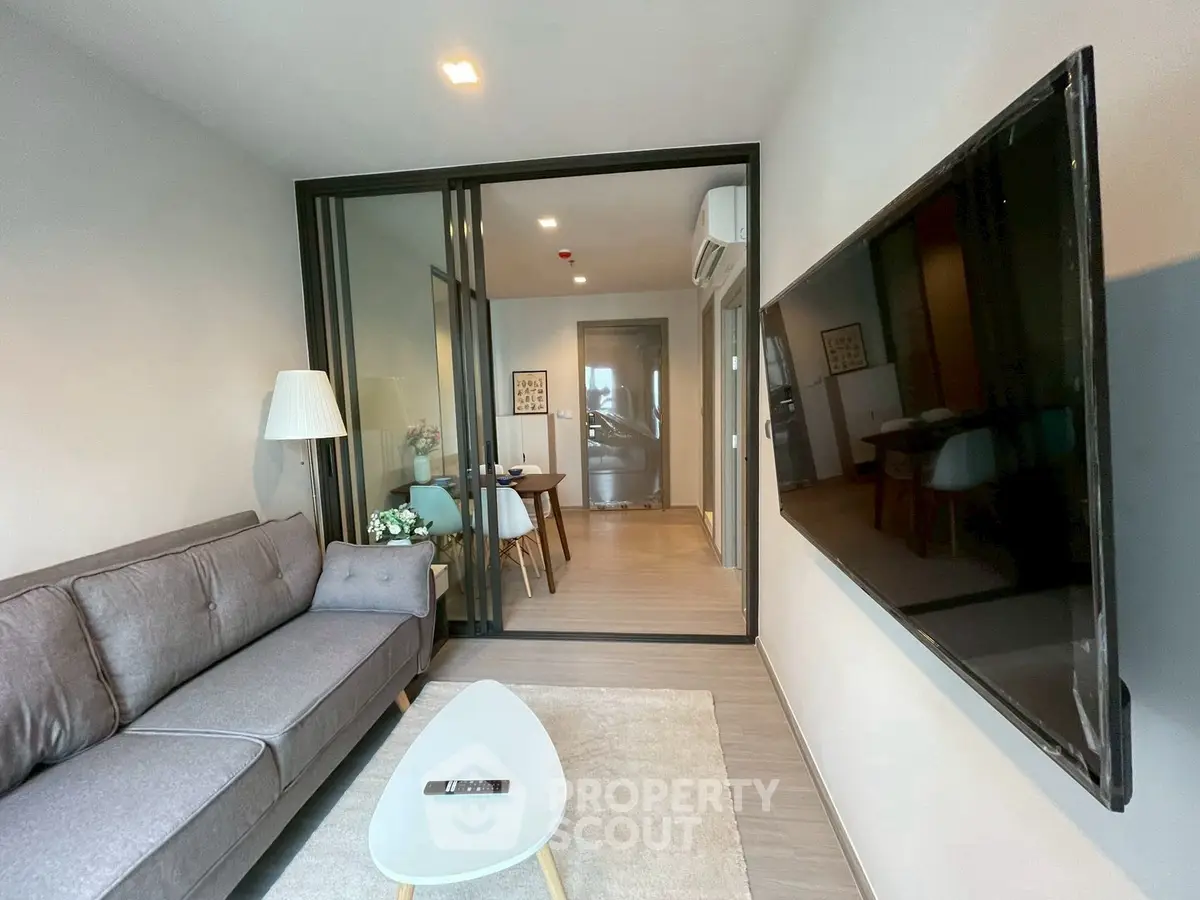 Modern living room with sleek design and large TV, featuring a cozy gray sofa and stylish decor.