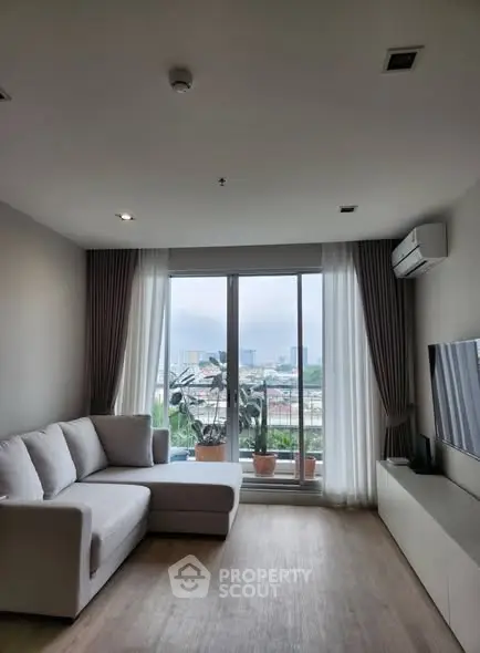 Modern living room with large window and city view, featuring a cozy sofa and sleek TV unit.