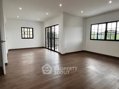 Spacious living room with large windows and wooden flooring, perfect for natural light and modern living.