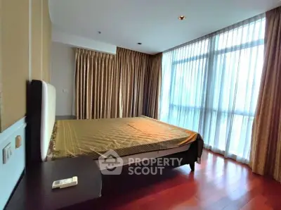 Spacious bedroom with large windows and elegant curtains, featuring a cozy bed and wooden flooring.