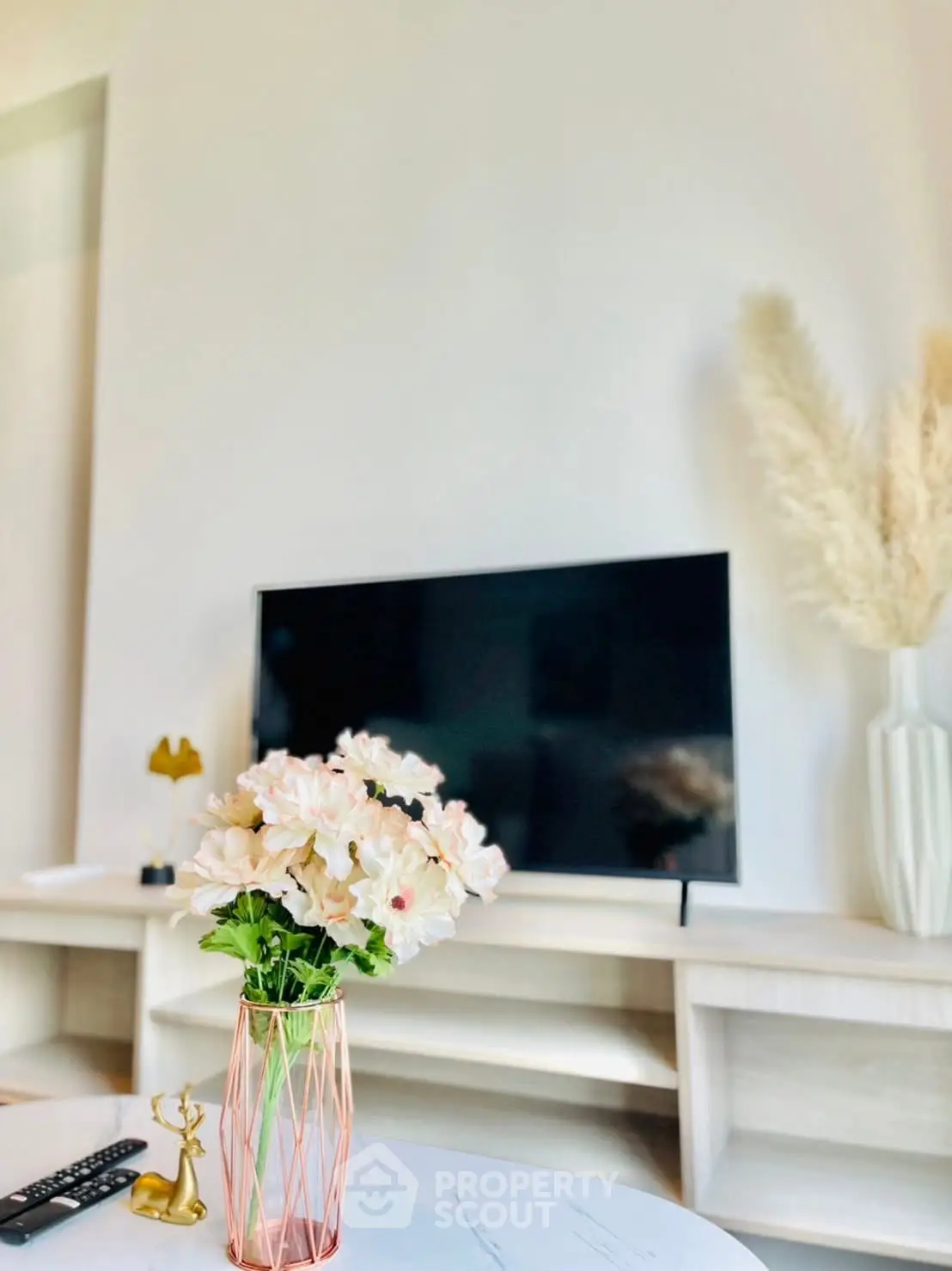 Modern living room with stylish decor and flat-screen TV, featuring elegant flower arrangement and sleek furniture.
