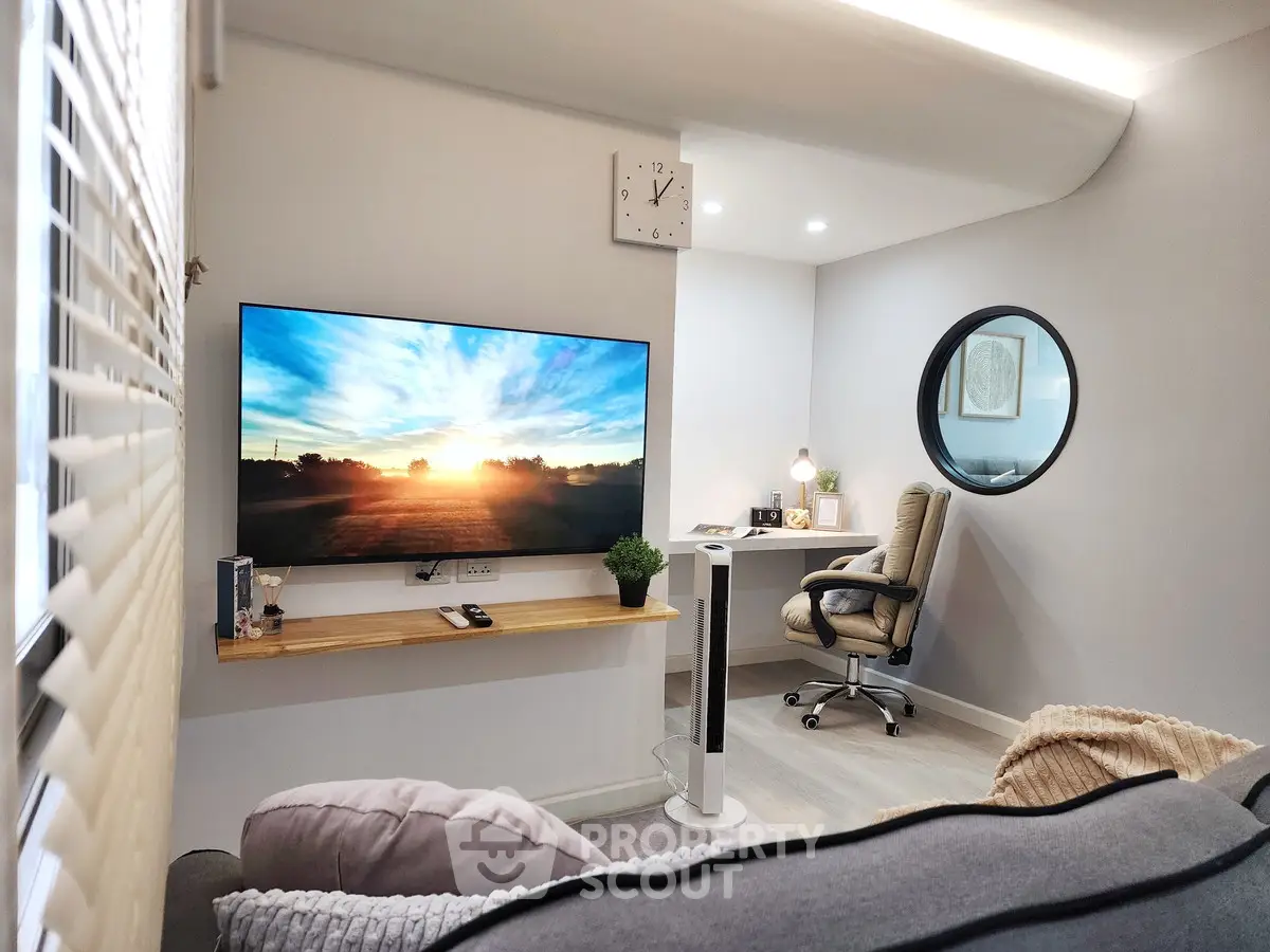 Modern living room with large TV and cozy workspace, featuring stylish decor and natural lighting.