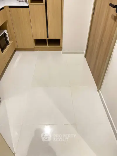 Modern kitchen with sleek cabinetry and microwave, featuring clean white tiled flooring.