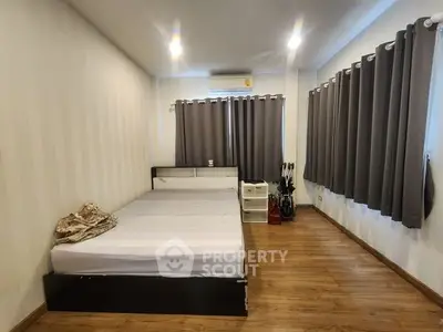 Spacious bedroom with wooden flooring and modern decor, featuring large windows with grey curtains.