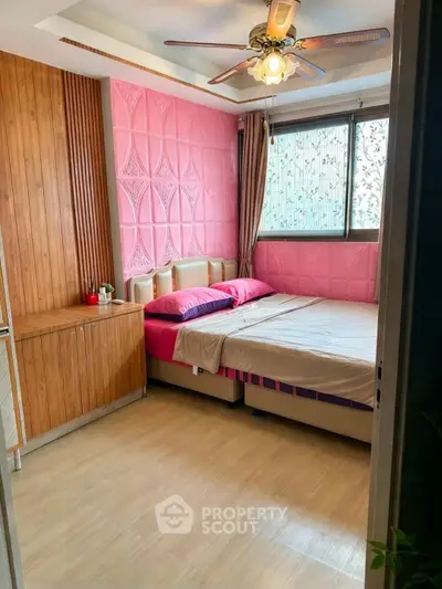 Charming bedroom with pink accent wall and ceiling fan, perfect for cozy living.