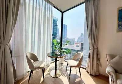 Bright corner unit with floor-to-ceiling windows and city view, featuring elegant seating area.