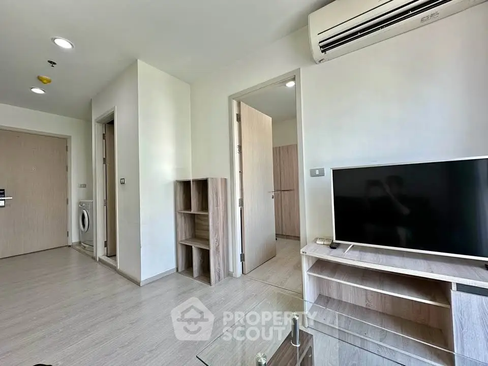 Modern living room with sleek design, featuring a TV, air conditioning, and light wood furnishings.
