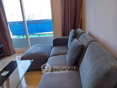 Spacious living room with modern grey sofa and glass coffee table, featuring a balcony view.