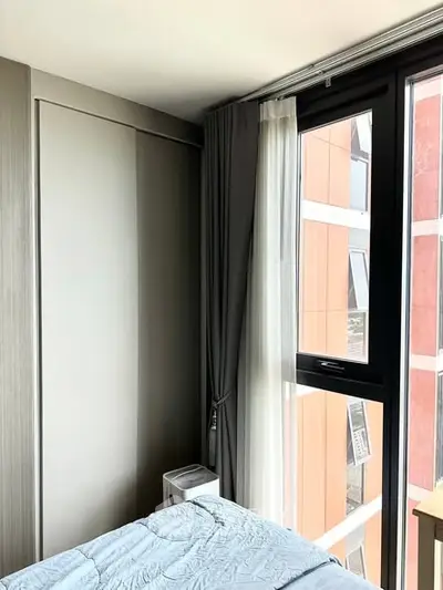 Modern bedroom with large window and stylish curtains, offering a glimpse of urban architecture outside.