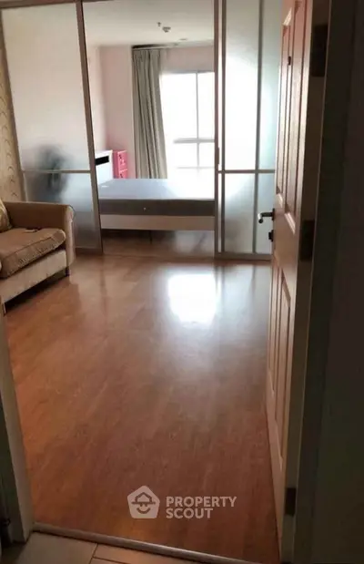 Spacious bedroom with sliding glass doors and wooden flooring, featuring a cozy sofa and ample natural light.