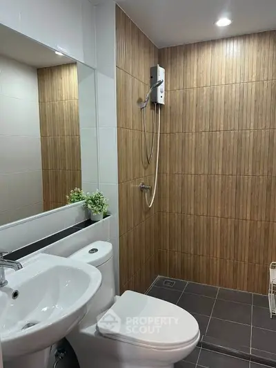 Modern bathroom with sleek fixtures and wood panel accents, featuring a shower and toilet.