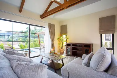 Spacious living room with large windows and pool view, featuring cozy gray sofas and wooden beams.