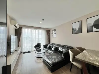 Modern living room with sleek black leather sofa and large windows offering city views.