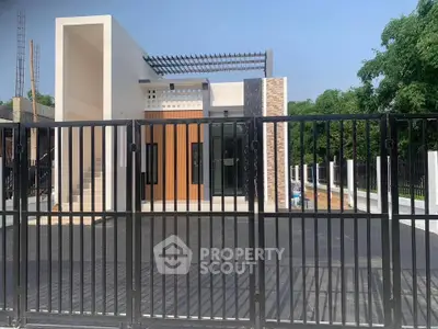 Modern minimalist house exterior with sleek design and gated entrance, surrounded by lush greenery.