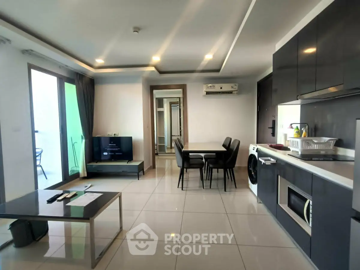 Modern open-layout living room with sleek kitchen, dining area, and balcony access in a stylish apartment.