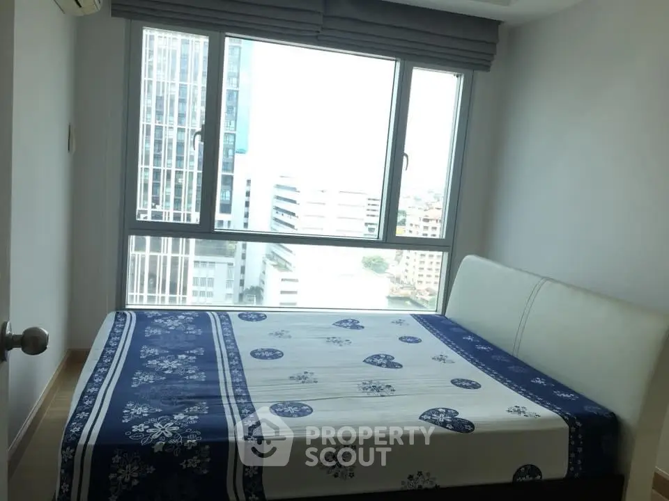 Modern bedroom with large window offering city view in high-rise apartment.