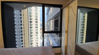 Modern bedroom with city view through large window in high-rise building.