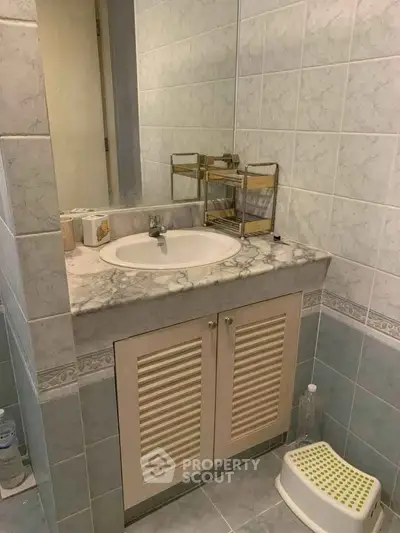 Compact bathroom with marble sink and tiled walls, featuring a small step stool and toiletries.