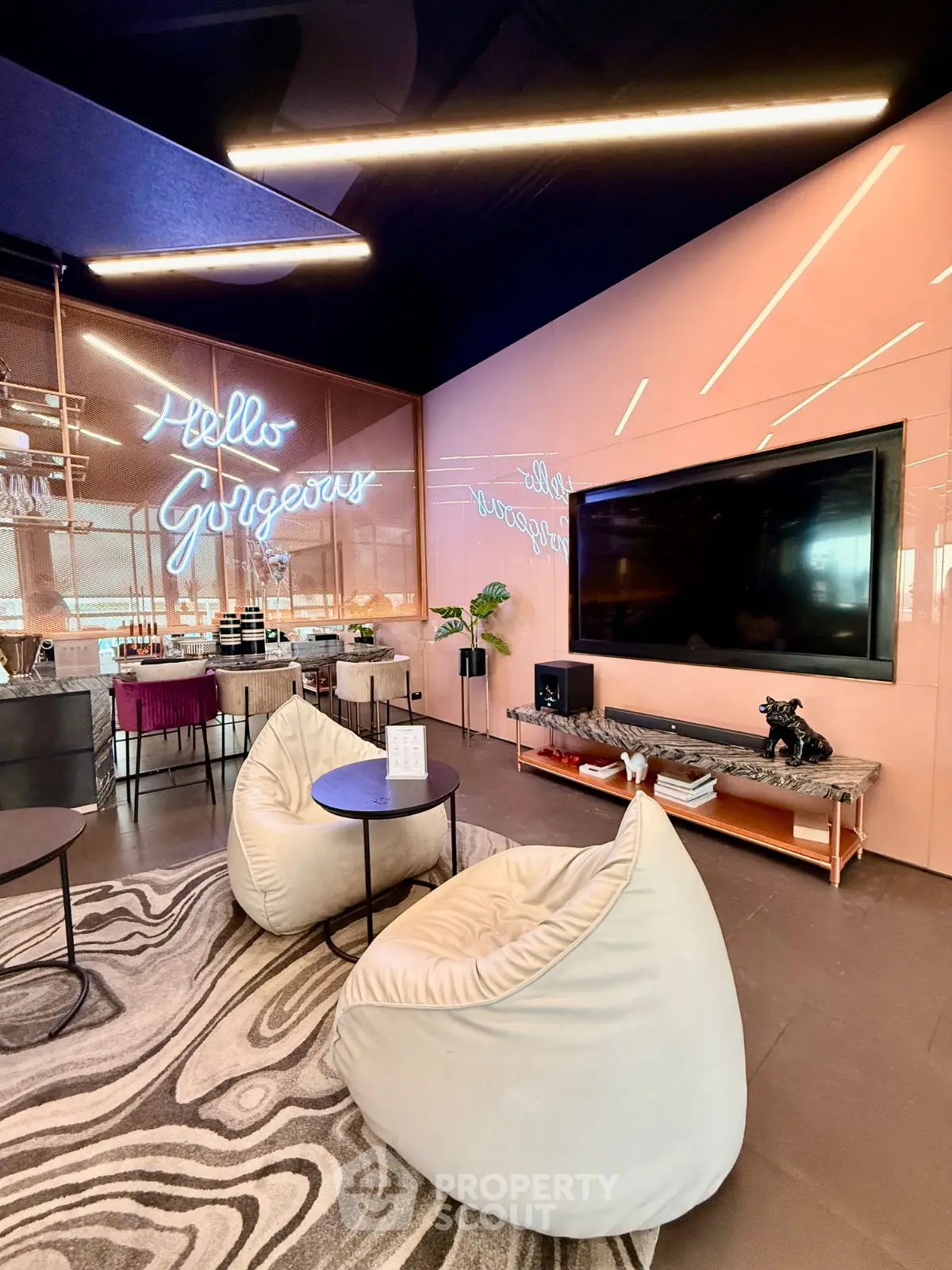 Modern living room with stylish decor, featuring bean bag chairs, large TV, and neon wall art.