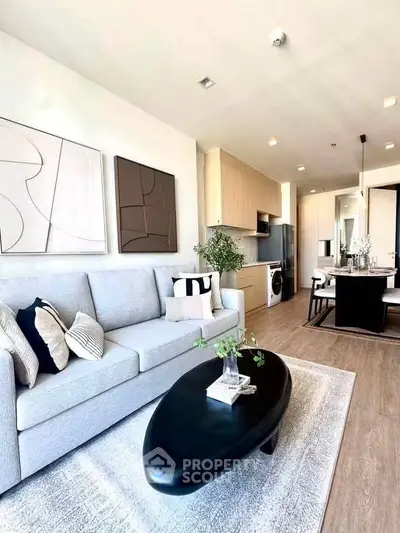 Modern open-plan living room with stylish decor and kitchen area, featuring sleek furniture and natural light.