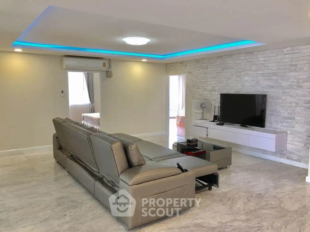 Spacious modern living room with sleek leather sofa and stylish TV setup, featuring ambient lighting and elegant flooring.