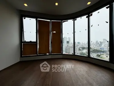 Spacious room with panoramic city view through large windows, featuring elegant wooden flooring.