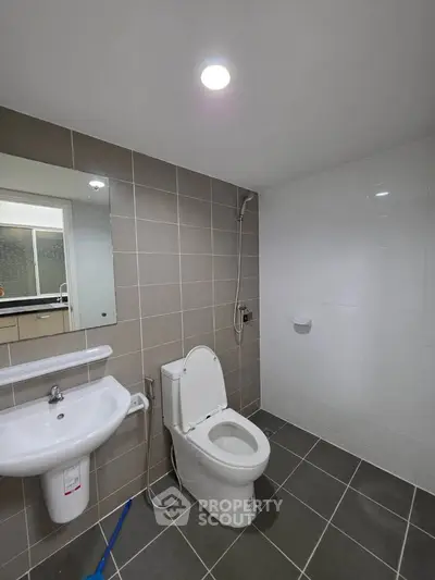 Modern bathroom with sleek fixtures and neutral tiles, featuring a toilet and sink.