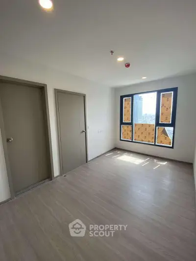 Spacious empty room with large window and modern flooring, ready for customization.
