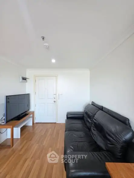Cozy living room with black leather sofa and flat-screen TV on wooden floor.