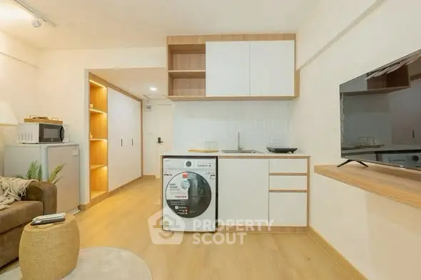 Modern studio apartment with stylish kitchen and cozy living area, featuring a washing machine and flat-screen TV.