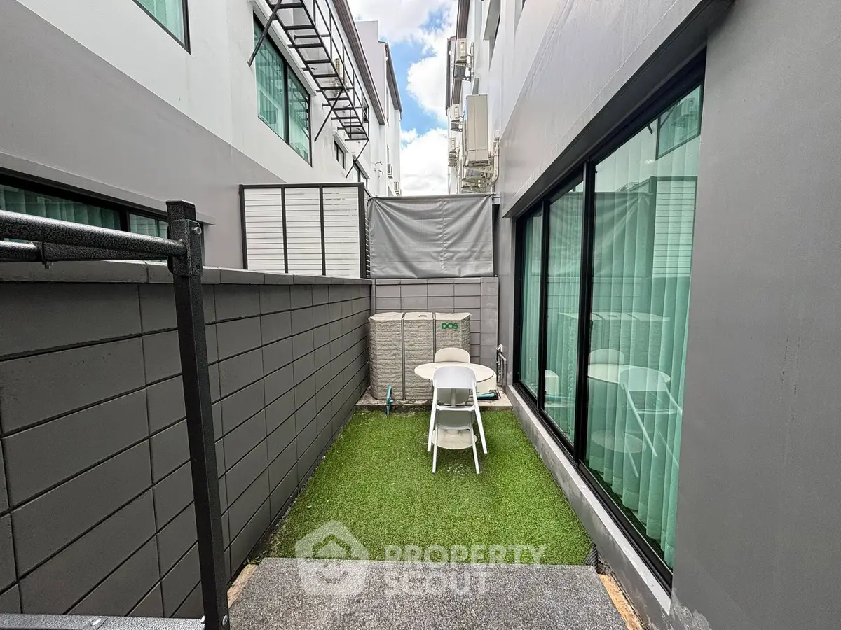 Charming outdoor patio with artificial grass and seating area in modern residential complex.