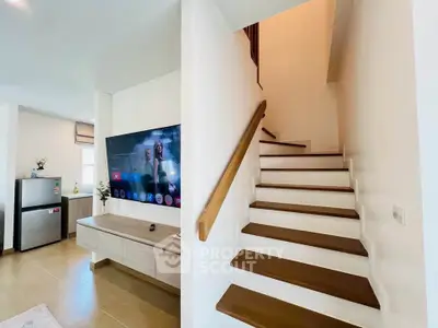 Modern living room with staircase and mounted TV, open layout with natural light.