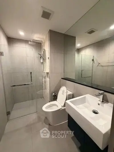 Modern bathroom with glass shower, sleek sink, and toilet in a contemporary apartment.
