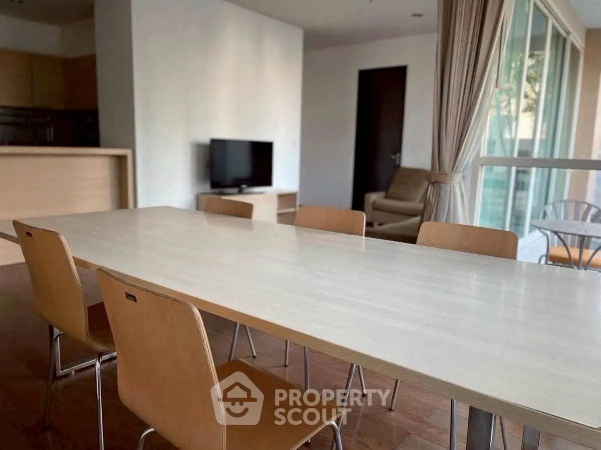 Spacious dining area with modern wooden table and chairs, adjacent to a cozy living room with natural light.