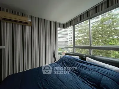 Modern bedroom with large windows and striped wallpaper, offering a city view.