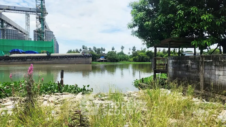 Scenic riverside view with lush greenery and industrial backdrop, perfect for serene living.