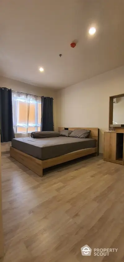 Spacious bedroom with modern wooden bed, matching sideboard, and elegant dark curtains complementing the warm-toned flooring.