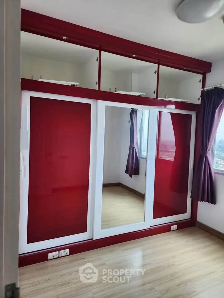 Spacious bedroom with red built-in wardrobe and large mirror, featuring wooden flooring and natural light.
