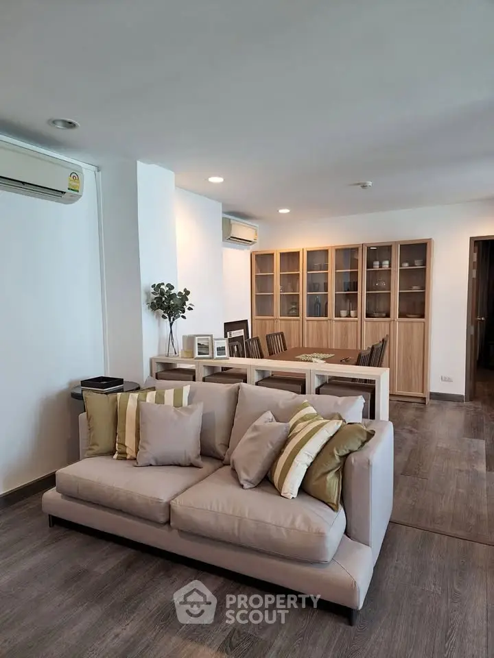 Spacious living room with modern decor and dining area, featuring elegant wooden flooring and stylish furniture.