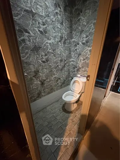 Compact bathroom with modern tiled walls and floor featuring a standard toilet.