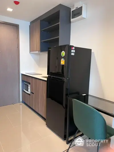 Modern kitchen with sleek black fridge and built-in microwave in compact apartment